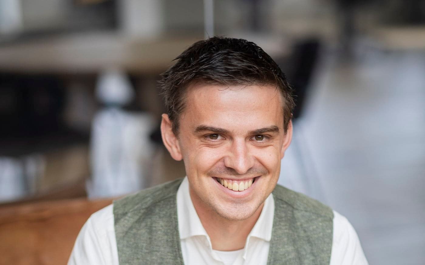 Glimlachende ondernemer zit met gevouwen handen aan tafel
