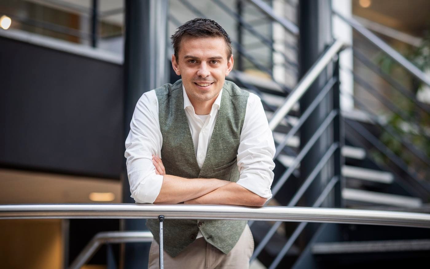 Ondernemer kijkt bedachtzaam vooruit, leunend bij de trap