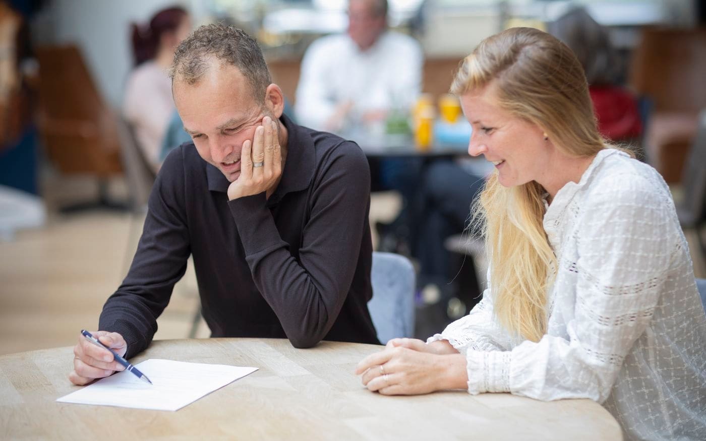 Twee mensen maken aantekeningen tijdens een gesprek aan tafel