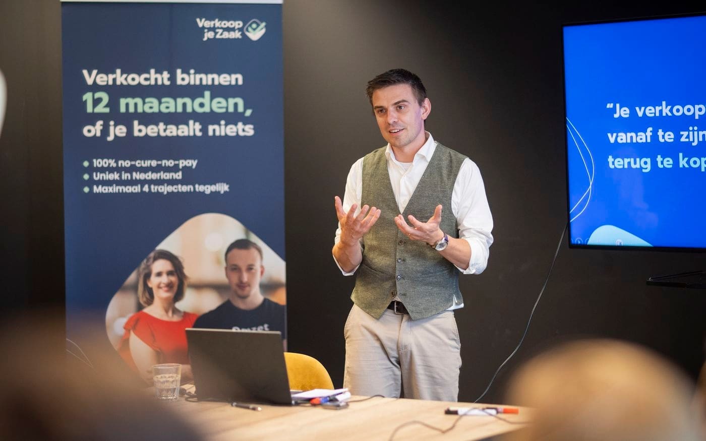 Maarten Ligthart presenteert naast de banner in de zaal