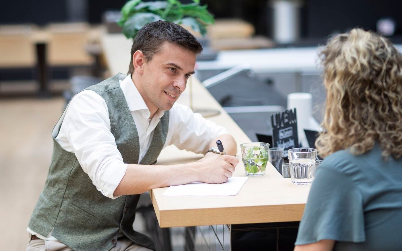 Adviseur maakt een aantekening tijdens een gesprek aan de statafel