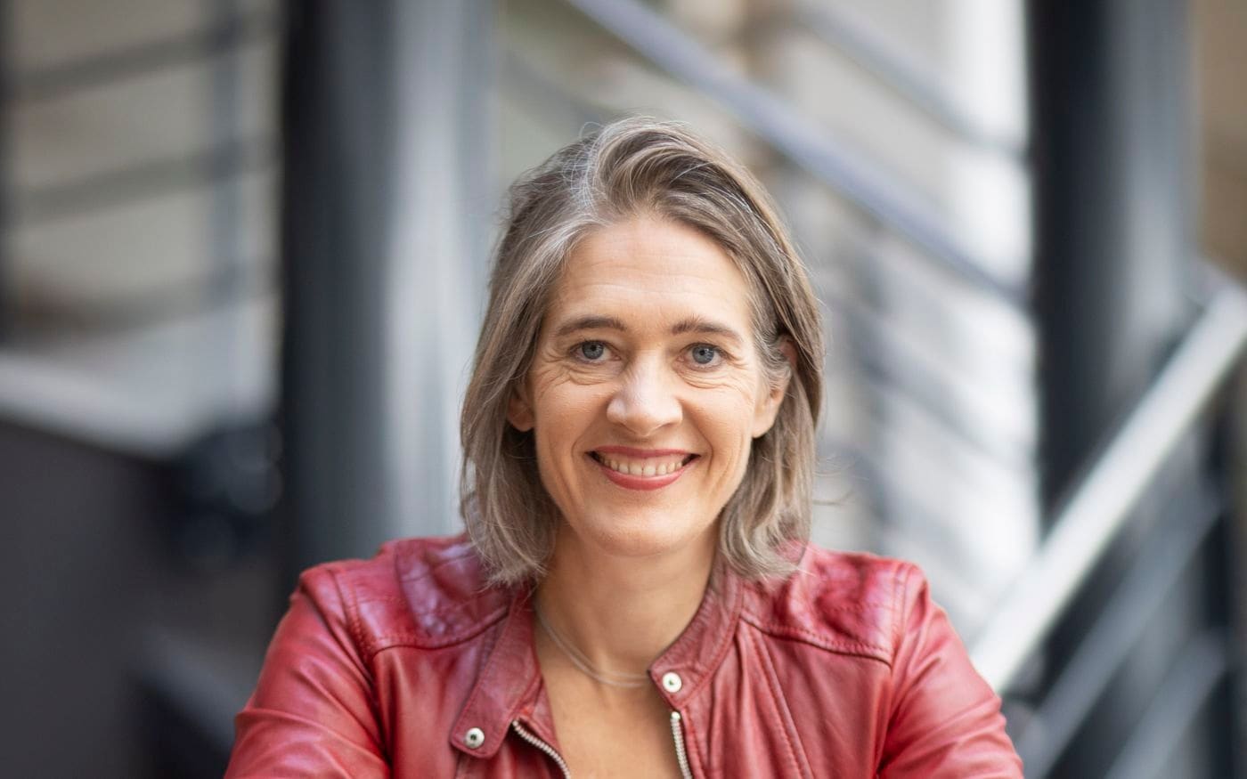 Onderneemster in een rood jasje leunt zelfverzekerd op de reling