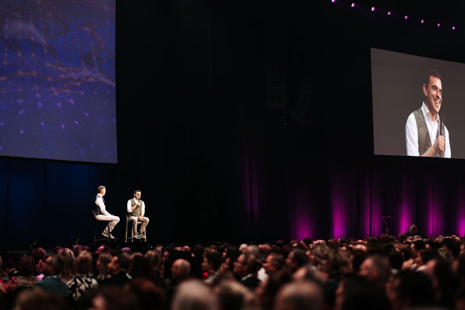 Maarten Ligthart wordt door Michael Pilarczyk geïnterviewd op het podium van Maximum Potential 2025, voor een volle zaal en met zijn gezicht groot op het videoscherm
